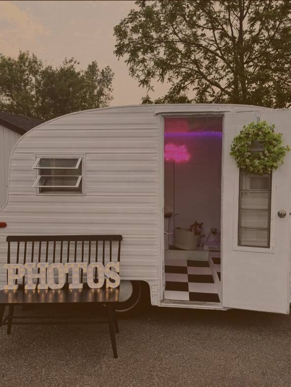 Vintage mobile camper photo booth with its door open and illuminated photo area inside